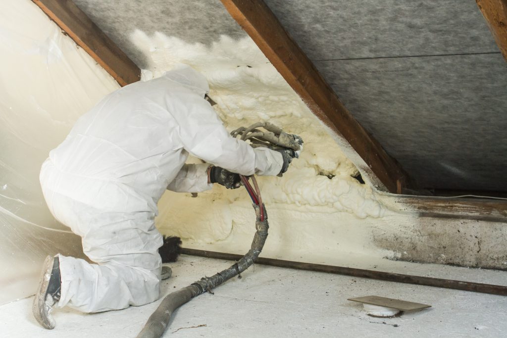 spray polyurethane foam for roof - technician spraying foam insulation using plural component gun for polyurethane foam, inside